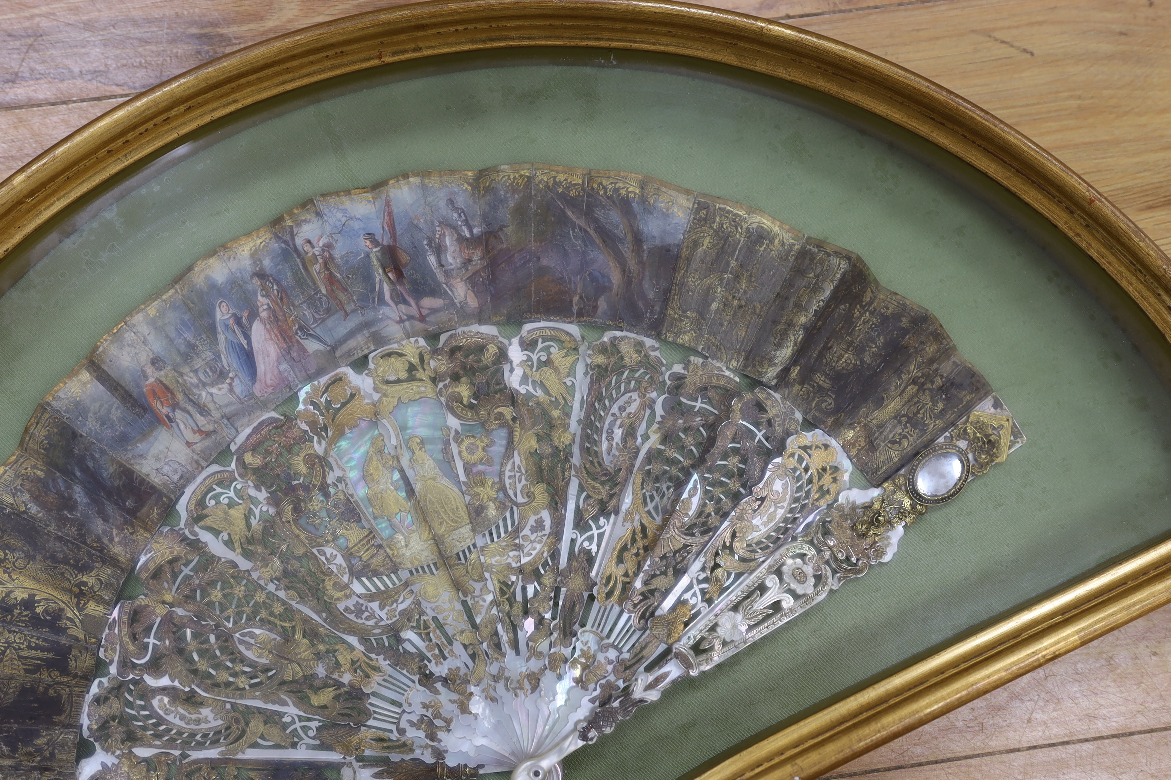 A cased early 19th century French painted paper leaf fan with gilt and mother of pearl sticks, fan 24cm high